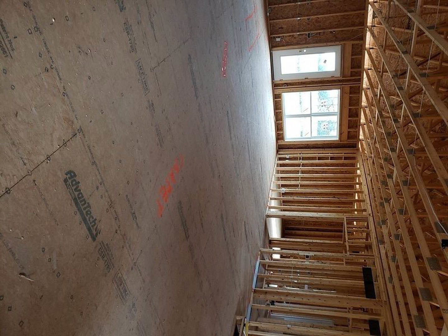 Exposed wood ceiling beams, square-paned window, light-colored walls, and partial view of wooden staircase in a custom home interior