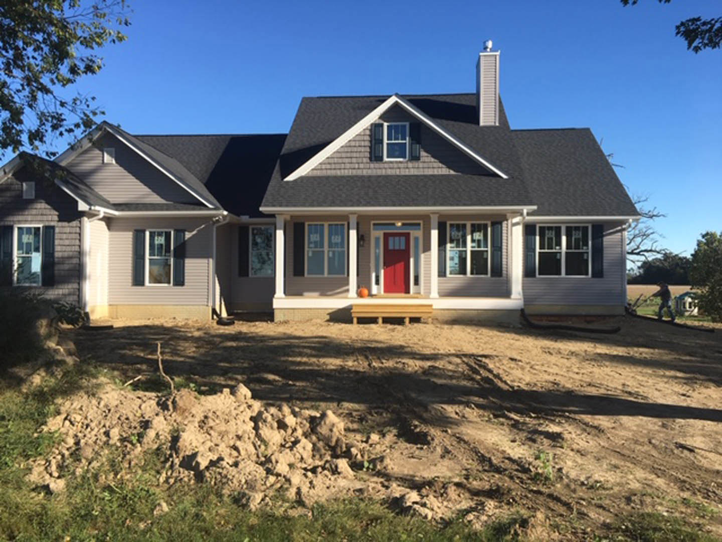 Two-story house with white siding, red front door, and white-framed windows, surrounded by a dirt patch and sparse landscaping.