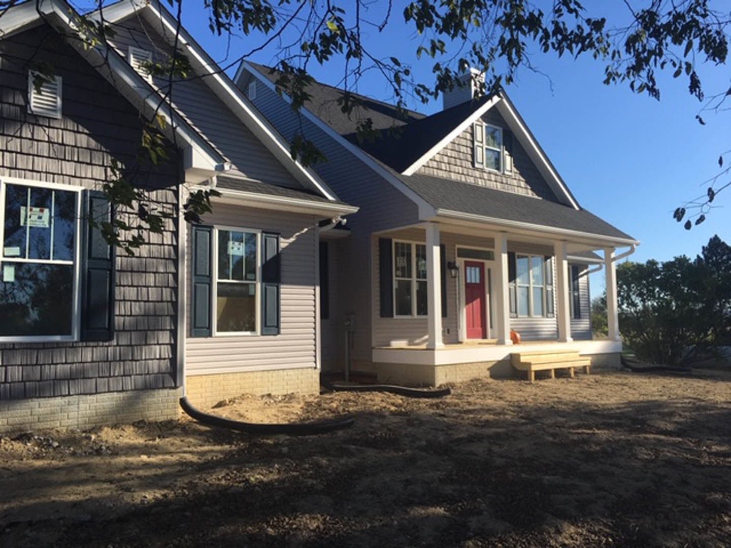Two-story house with white siding, red front door with white trim, porch, large windows, grassy yard, black hose on ground, mature trees in background