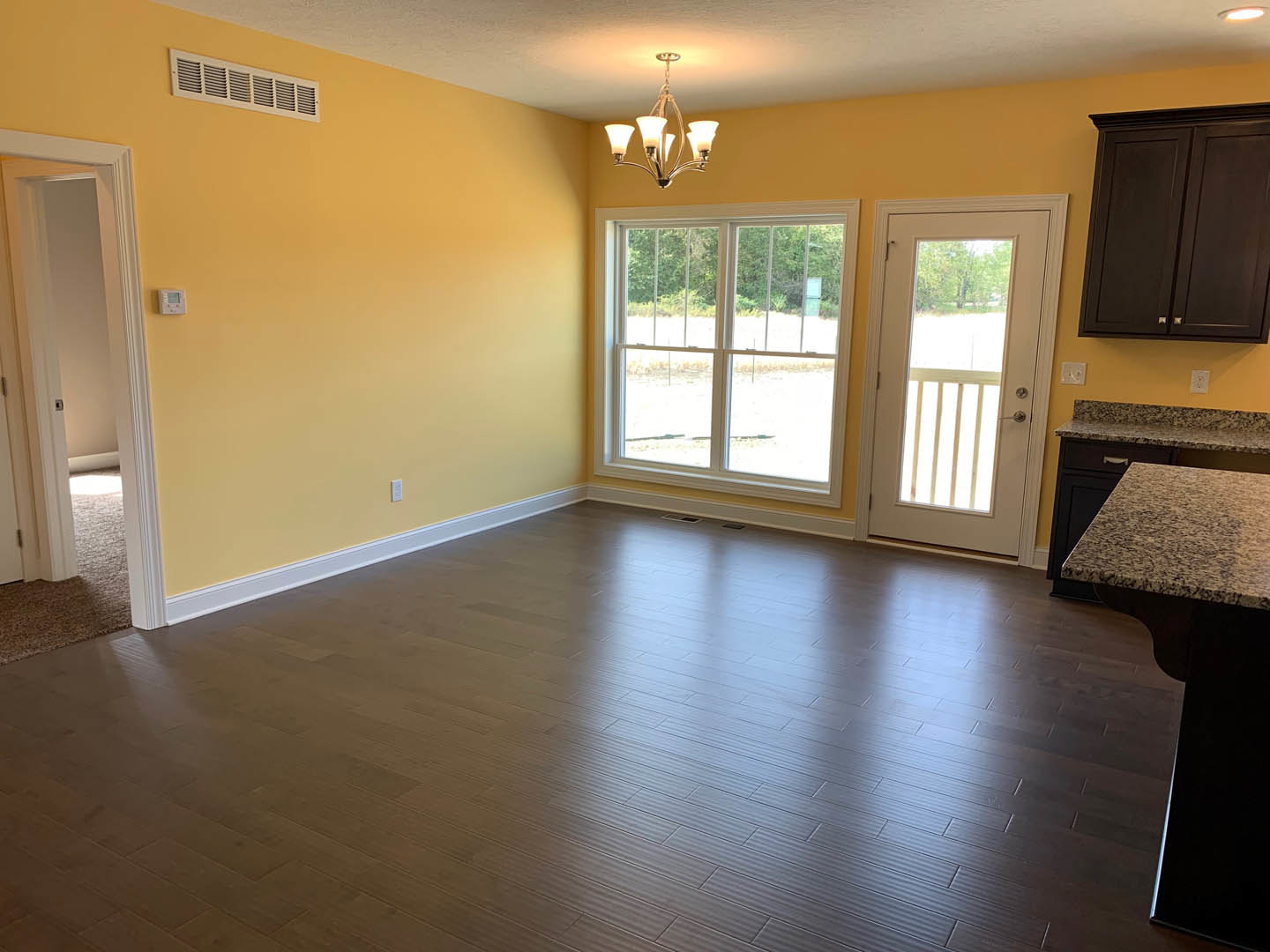 Wood flooring room with white walls, glass-paneled door, large window showing outdoor view, modern chandelier, and built-in cabinet.