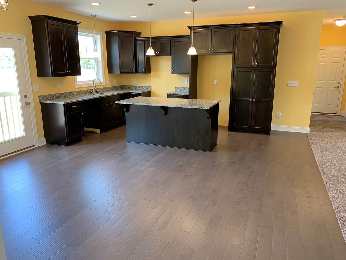 Spacious kitchen featuring a large marbled island countertop, dark wood cabinetry, and wide plank wood flooring