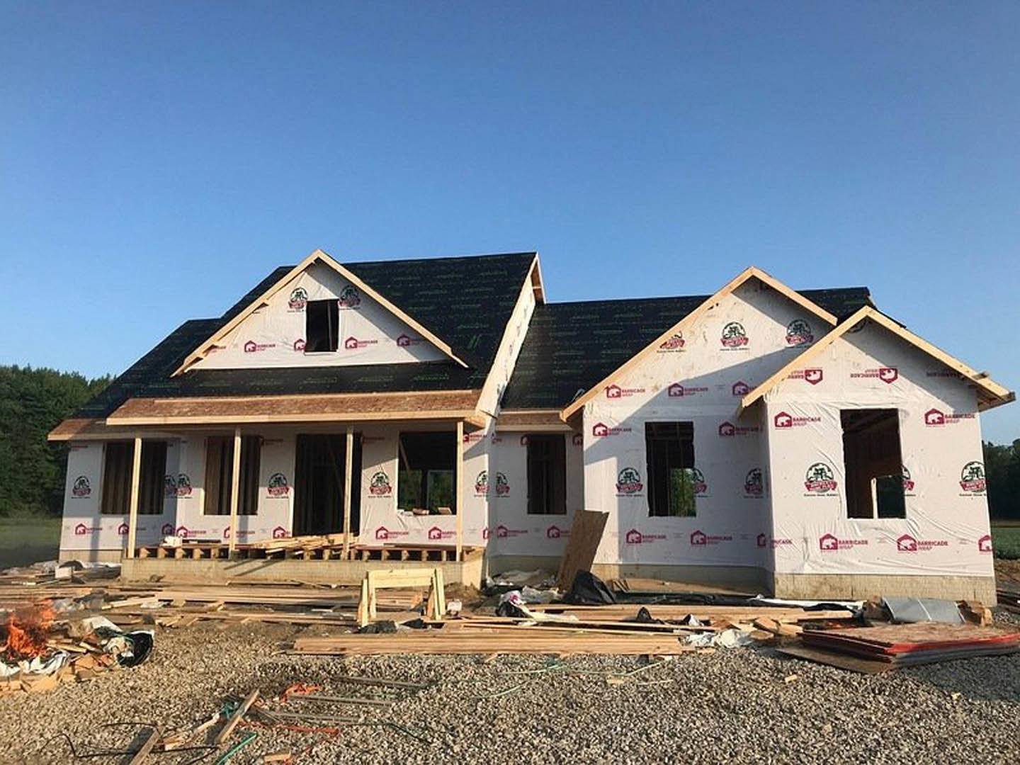 Framed wood structure of a house under construction with exposed beams and plywood, set against a clear blue sky