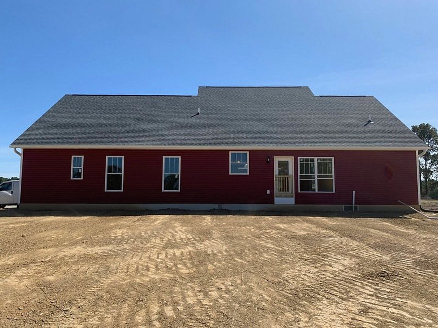Red siding house with white window trim and railing, red roof, dirt yard in foreground, tree branches visible against blue sky