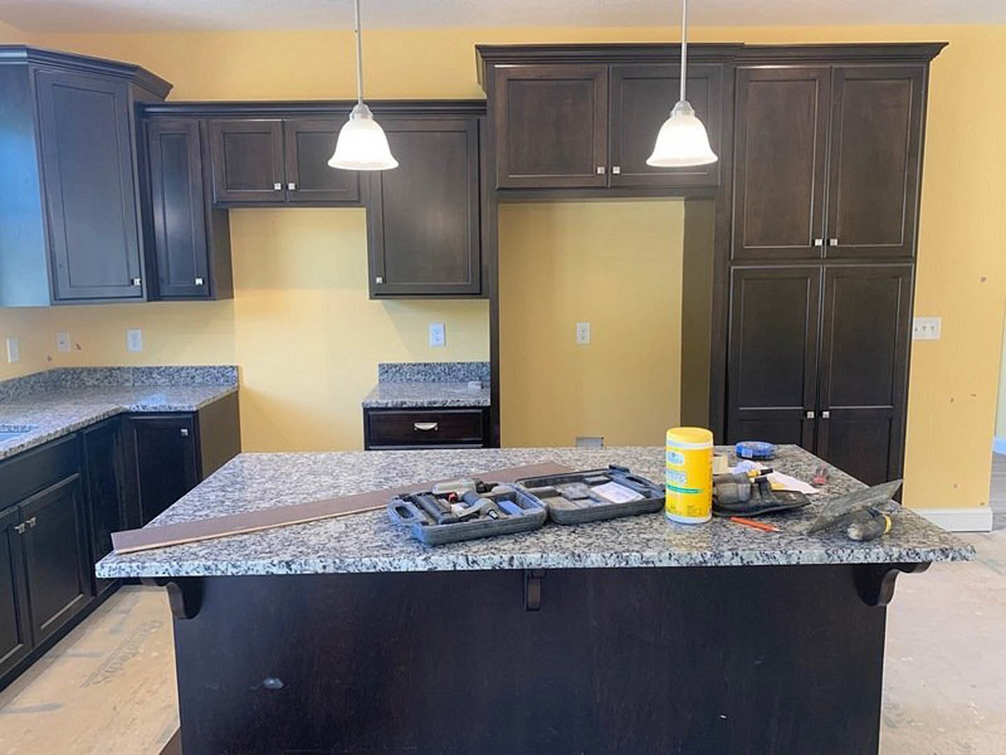 Modern kitchen with white cabinetry, stone countertop, stainless steel sink, toolbox and yellow container on counter, under-cabinet lighting, and open drawer