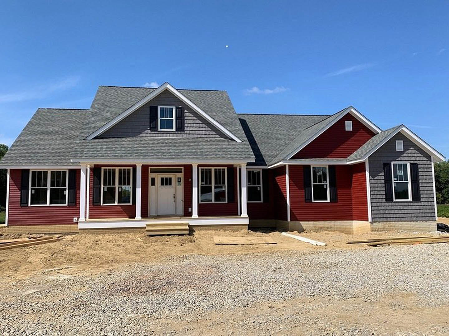 Red exterior wall with white trim, white door featuring glass panes, white-framed window, gravel and dirt covering ground, partially finished porch area