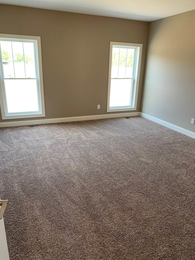 Neutral-toned carpeted floor, white walls, multiple large windows with white frames, natural light filling spacious room