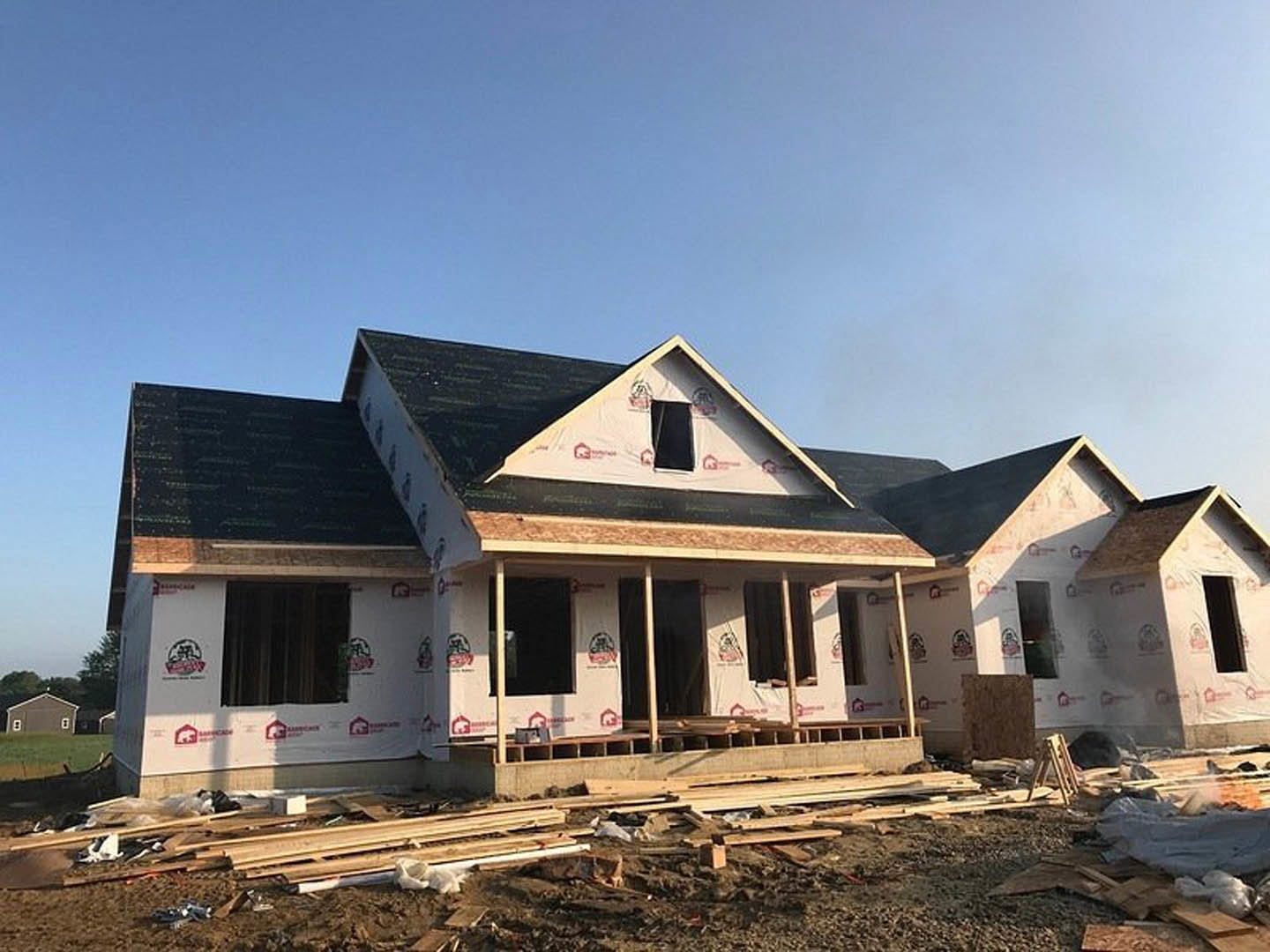 Framed house under construction with exposed wood beams, partially installed roof, and clear blue sky in background