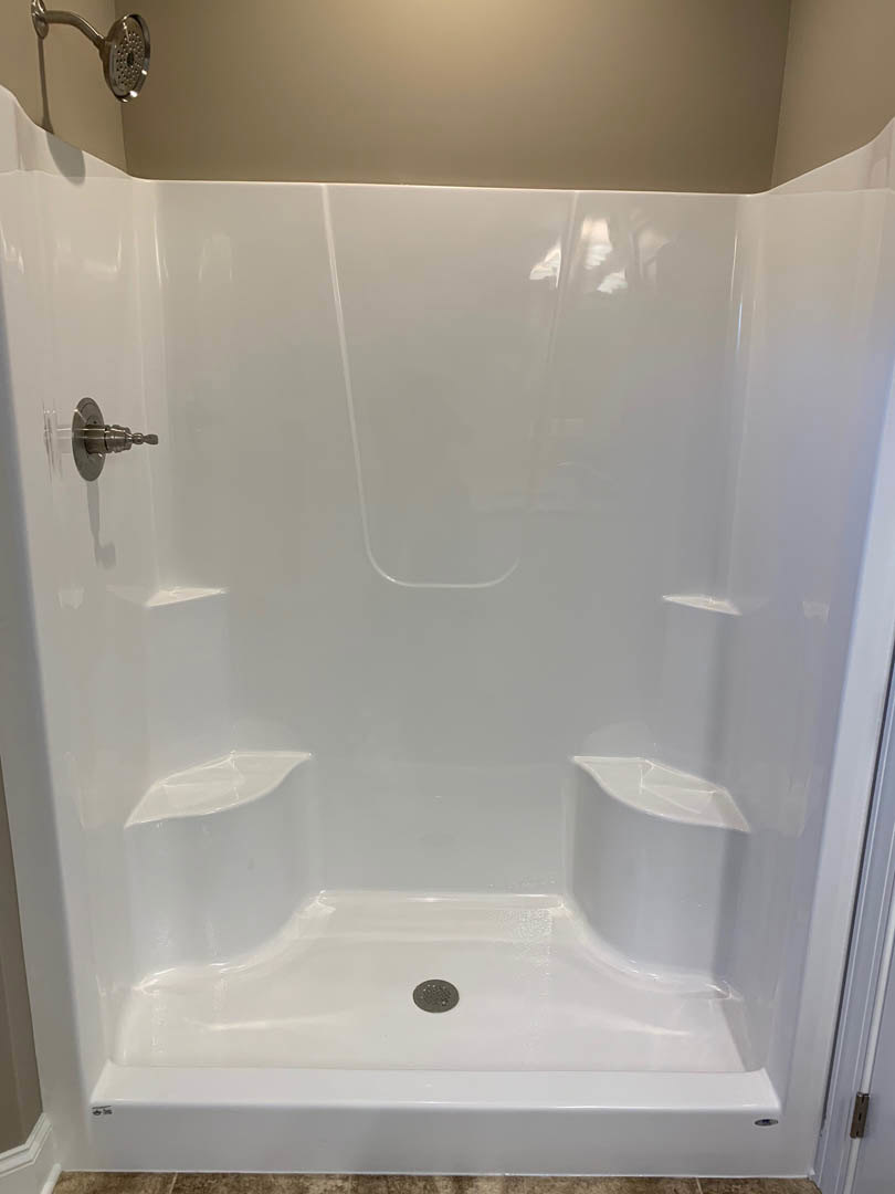 White tiled shower with silver handheld shower head and hose, black trim along wall, chrome faucet handle.