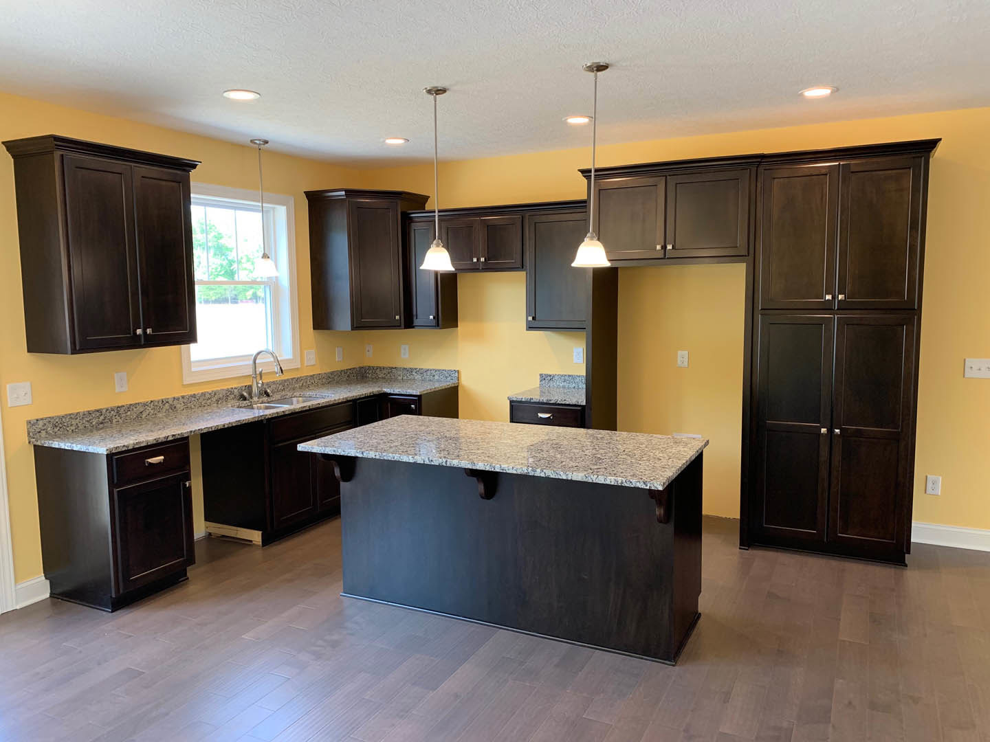 Marble countertop with stainless steel faucet, dark wood cabinets, and window with overhead lighting in a modern kitchen