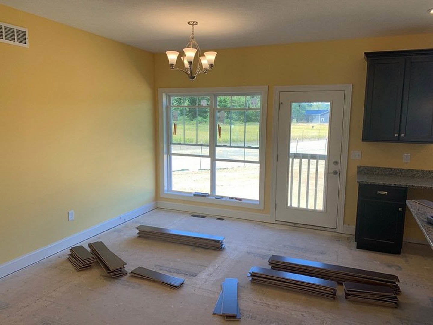 Laminate flooring in a den with white-framed window, glass-paneled door, black cabinet with drawer, and chandelier lighting