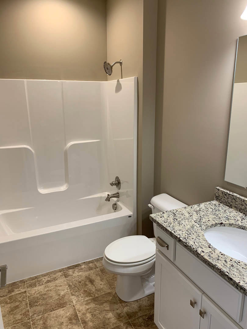 Modern bathroom featuring a white freestanding bathtub, wall-mounted sink with chrome faucet, and sleek toilet against white tile walls with grey trim