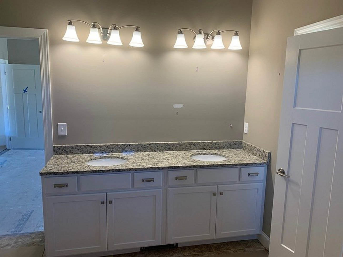 Bathroom with double vanity sinks, white cabinetry, granite countertops, modern bell-shaped light fixture, and a door leading to an adjacent room.