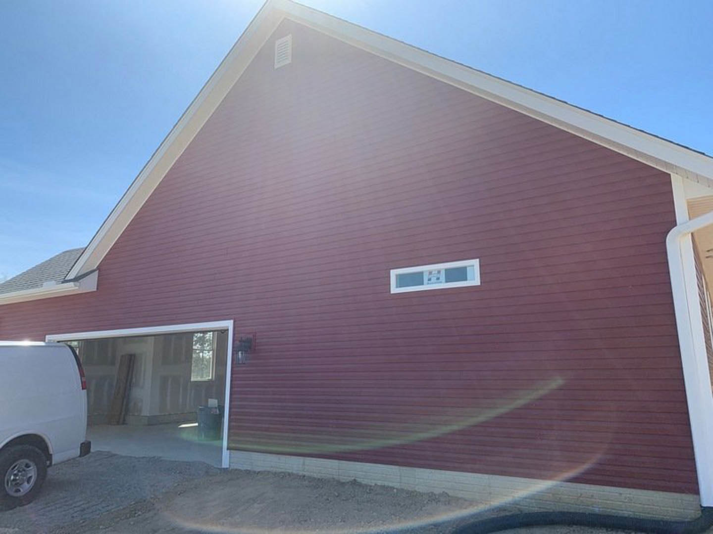 Red barn-style home with large garage door, white trim, and square window; white van parked beside building, tire visible in foreground