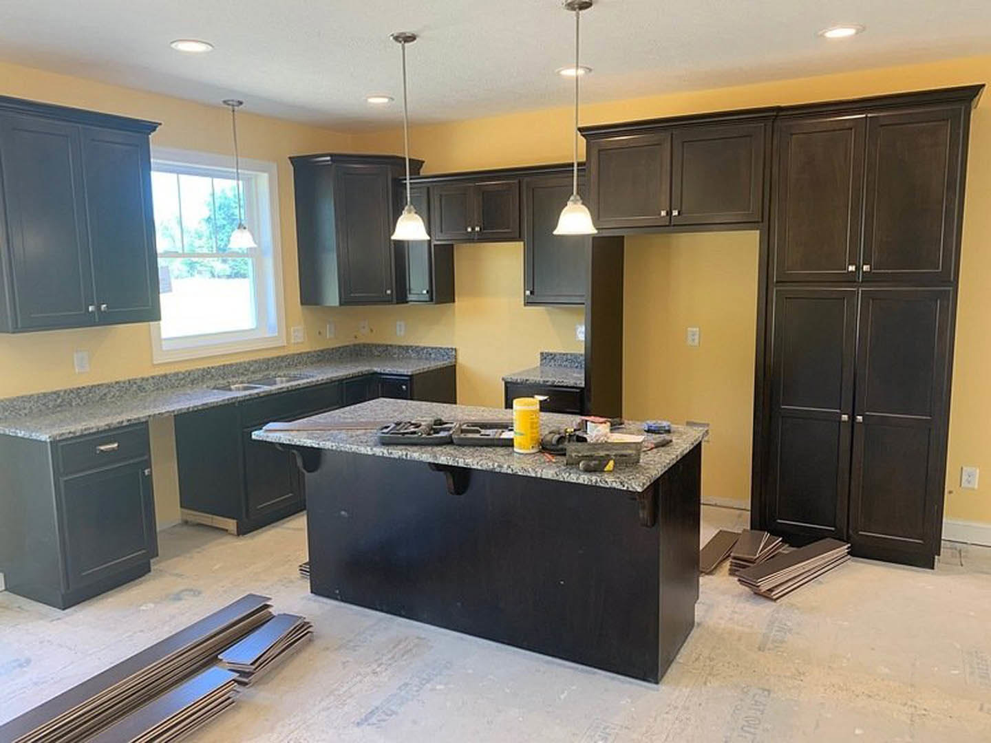 Modern kitchen with white cabinetry, stone countertop, stainless steel sink, assorted tools and yellow bottle on counter, natural light streaming through window, wood flooring