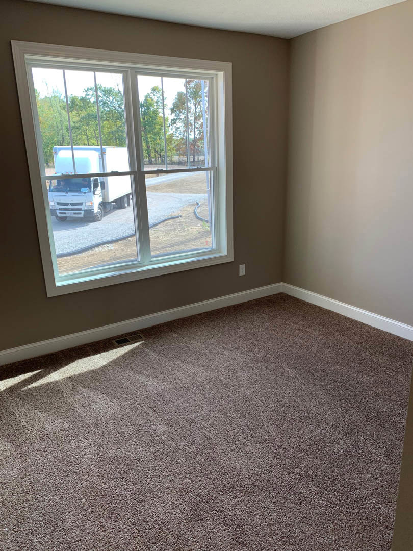 Carpeted room with large window overlooking street, white truck visible outside, neutral walls and laminate flooring near window