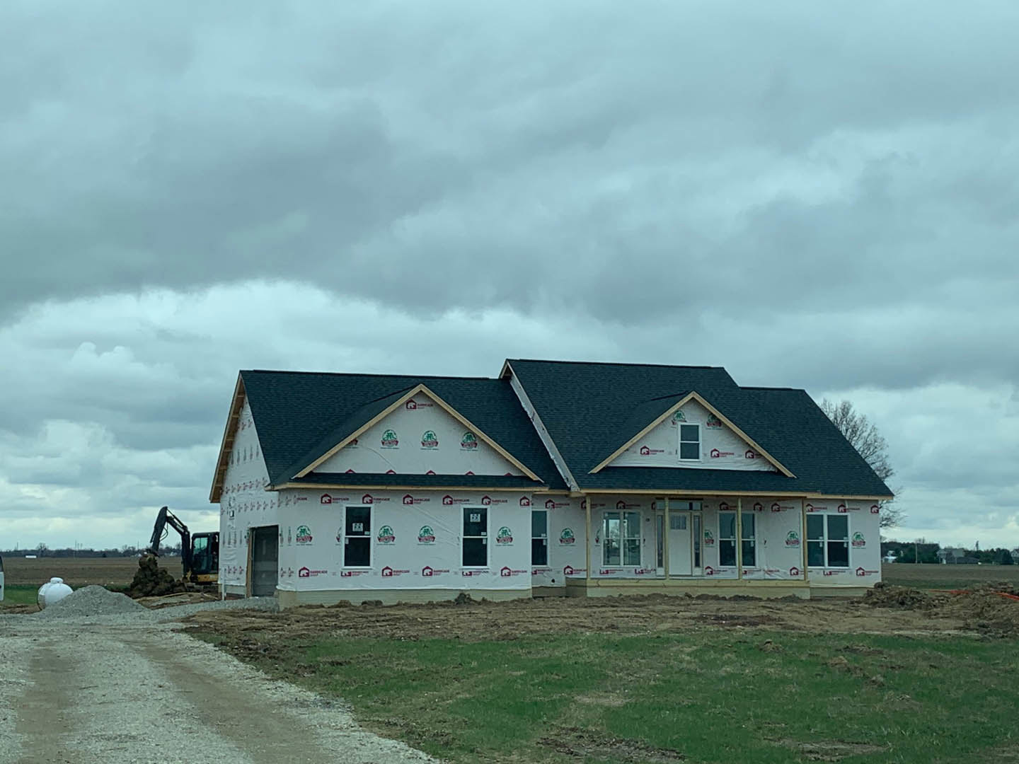 White-sided house under construction with crane overhead, cloudy sky, grassy foreground, white door displaying a sign