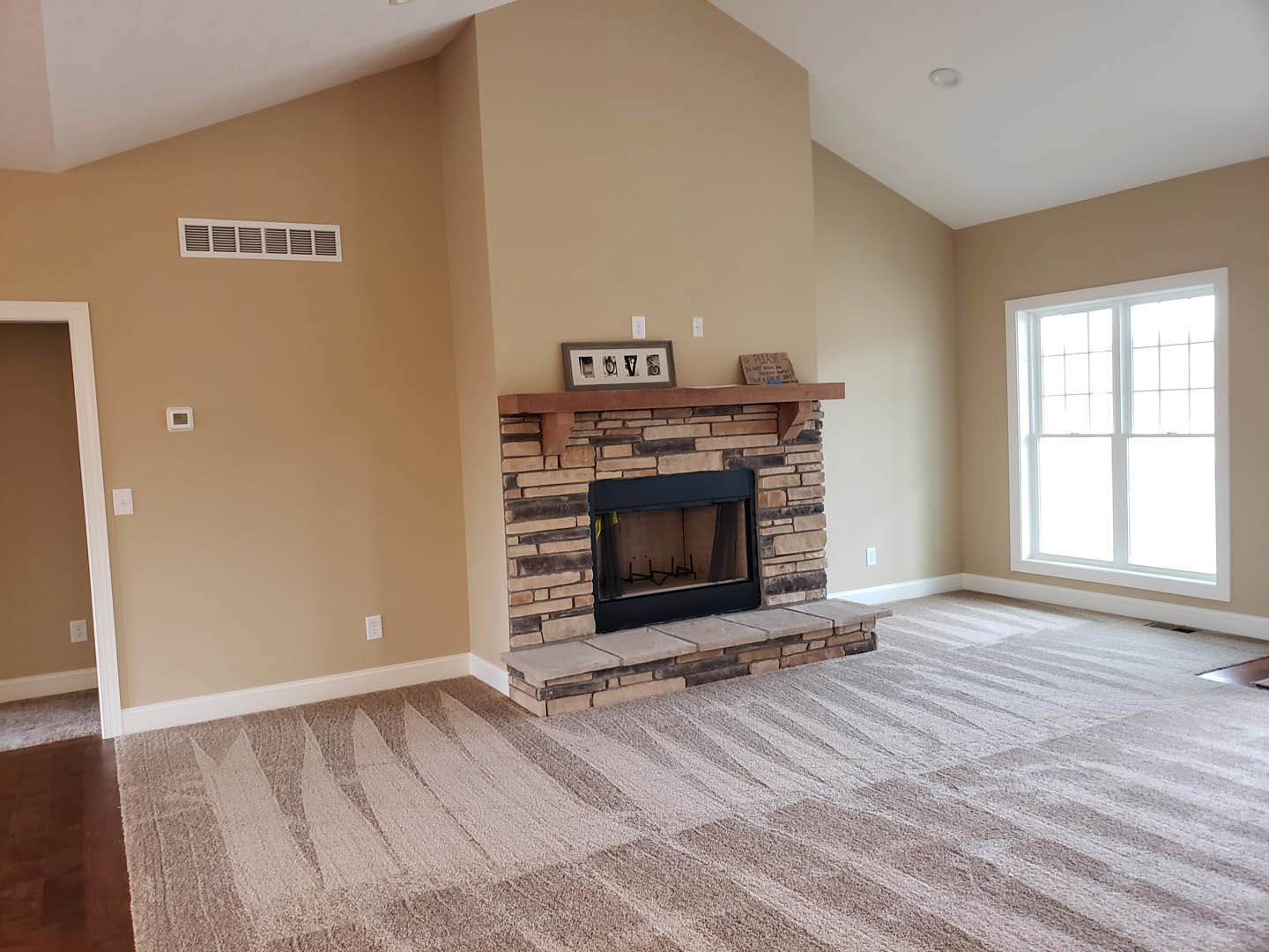 Carpeted living room featuring a black-framed fireplace with a picture frame on the mantle, large window, and neutral wall finishes.