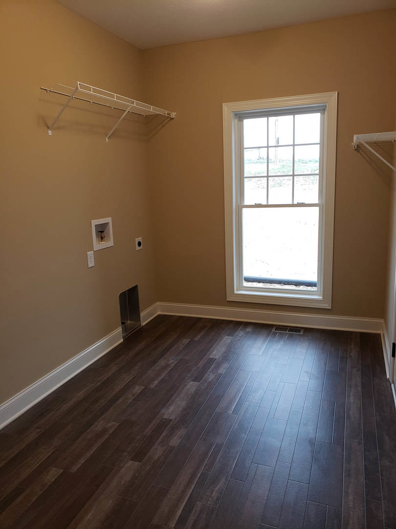 Corner room with white-framed window, hardwood floor with vent, white metal shelf mounted on wall, plaster walls, and built-in fire hydrant.