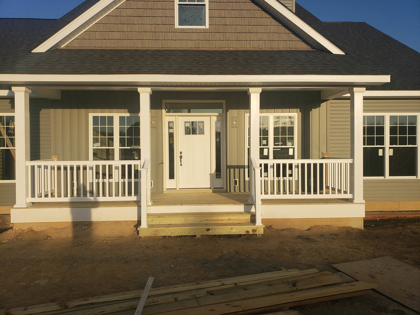 Front porch with white railing, white door with glass panes, white-framed window, wood siding, and blue sky in background