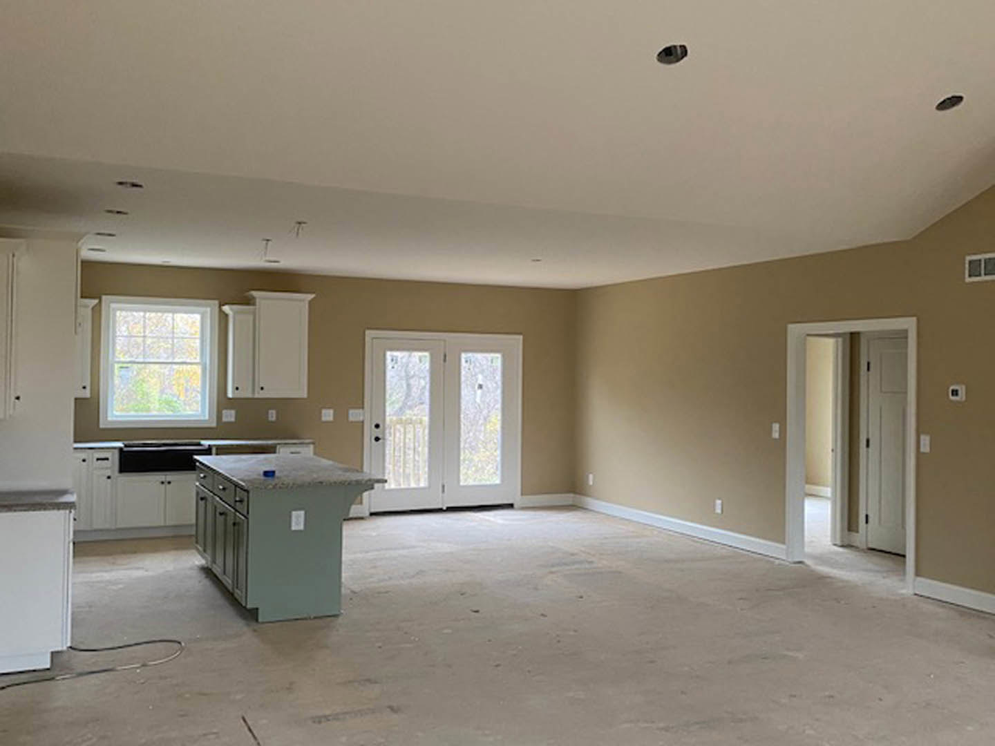Kitchen and dining room under construction with concrete floors, white walls, a kitchen island holding a blue object, white double doors with glass panels, doorway, multi-pane