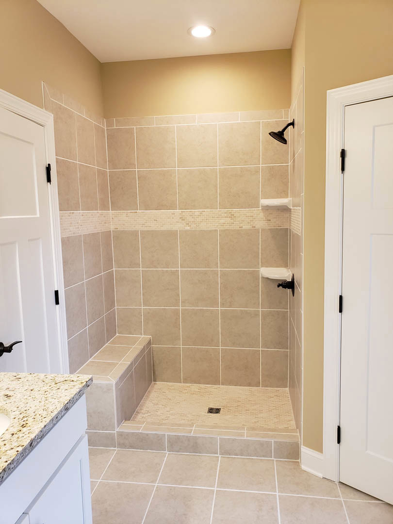Modern bathroom featuring a glass-enclosed shower with a chrome shower head mounted on a tiled wall, white countertop with integrated sink and sleek cabinetry, tile flooring, and