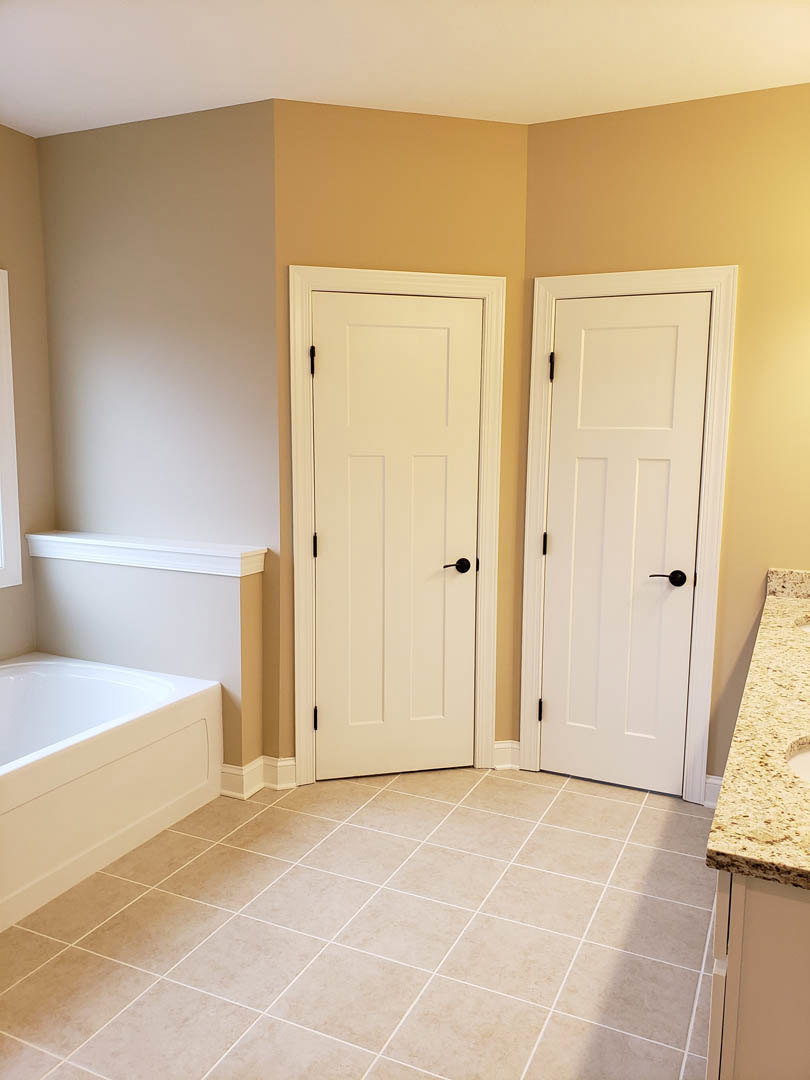 Bathroom featuring two white paneled doors with black handles, freestanding bathtub, light tile flooring, and stone countertop.
