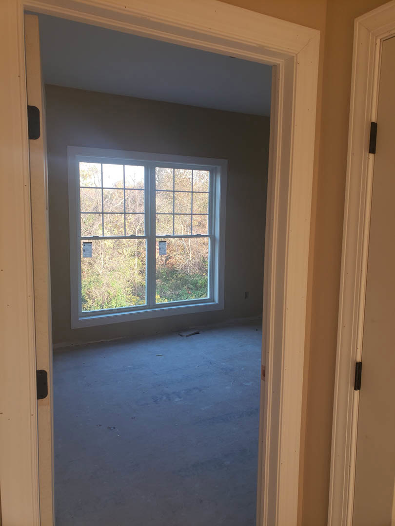 Concrete floor and white walls in a room with a large window framed in white, trees visible outside.