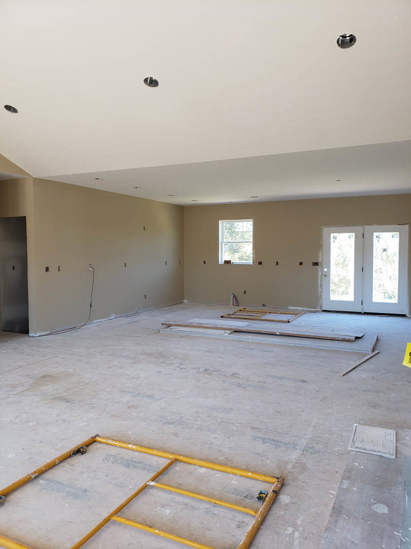 Room with grey plaster walls, double glass-panel doors, white-framed window, yellow sign, yellow pipe on floor, white door with window, and ceiling insulation visible.