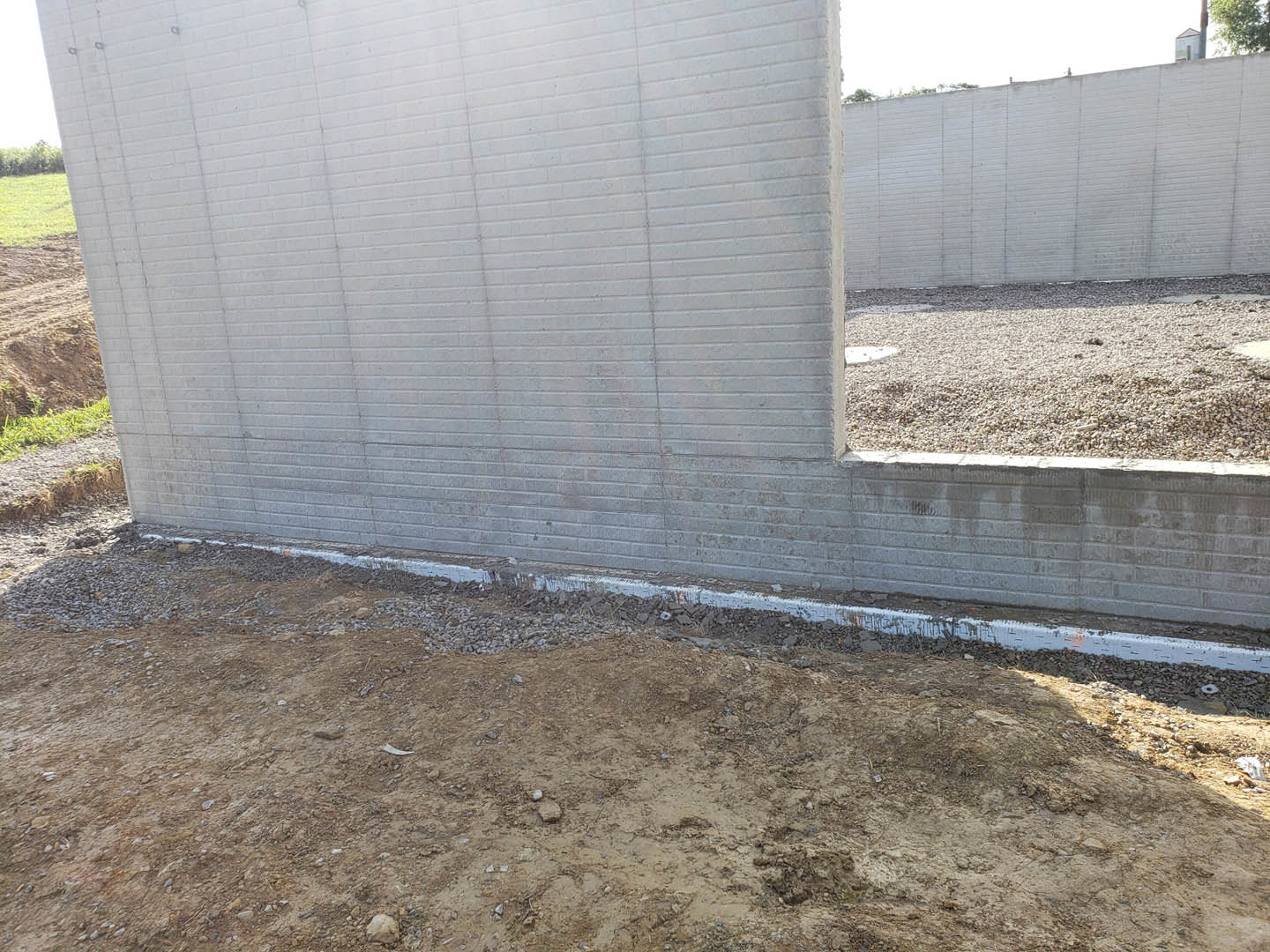 Red brick exterior wall with a large hole exposing underlying dirt and rocks, surrounded by scattered gravel and patches of grass.