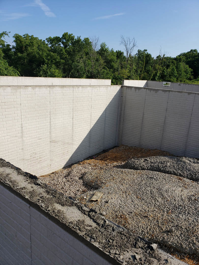 Concrete foundation surrounded by gravel, rocks, and dirt, with trees and blue sky in the background