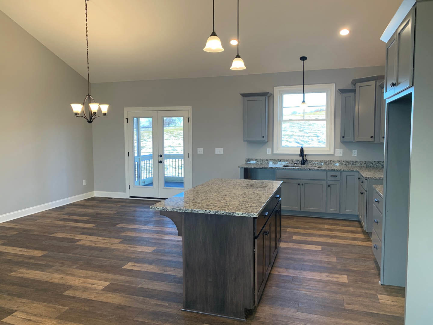 Spacious kitchen featuring a large marble-topped island, wood flooring, white cabinetry, double glass-panel doors, and a window allowing natural light