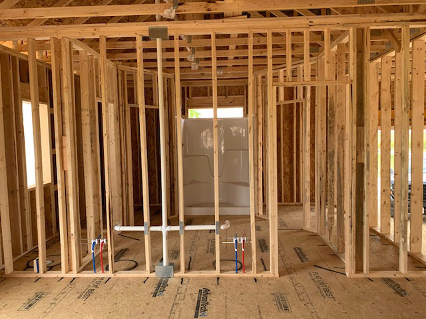 Bathroom under construction with exposed wooden ceiling beams, unfinished walls, and window; shower area visible with construction materials and insulation.