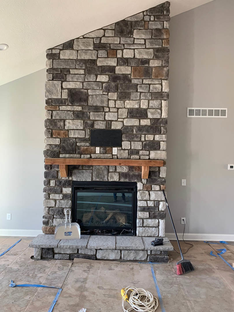 Stone fireplace with wood mantel, glass door and window, vacuum cleaner plugged into wall, white rectangular object with handle on floor, hardwood flooring