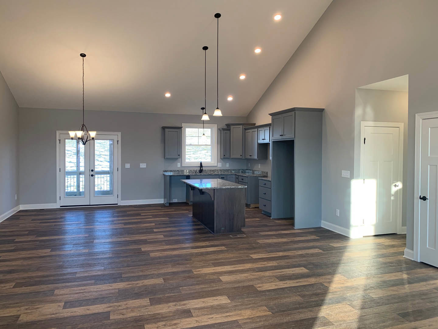 Spacious kitchen and living area featuring wood flooring, a central kitchen island with marble countertop, double glass doors, white door with sunlight streaming through, and