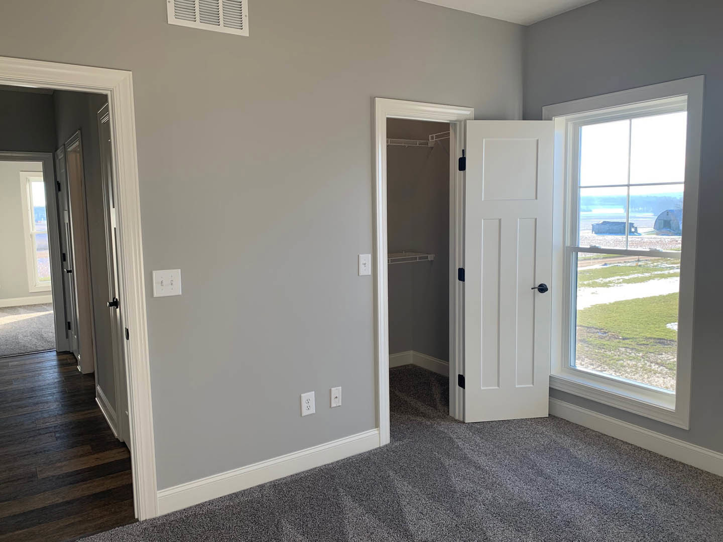 Dark wood flooring with white trim, open white door, window overlooking farm and barn, white light switch on wall