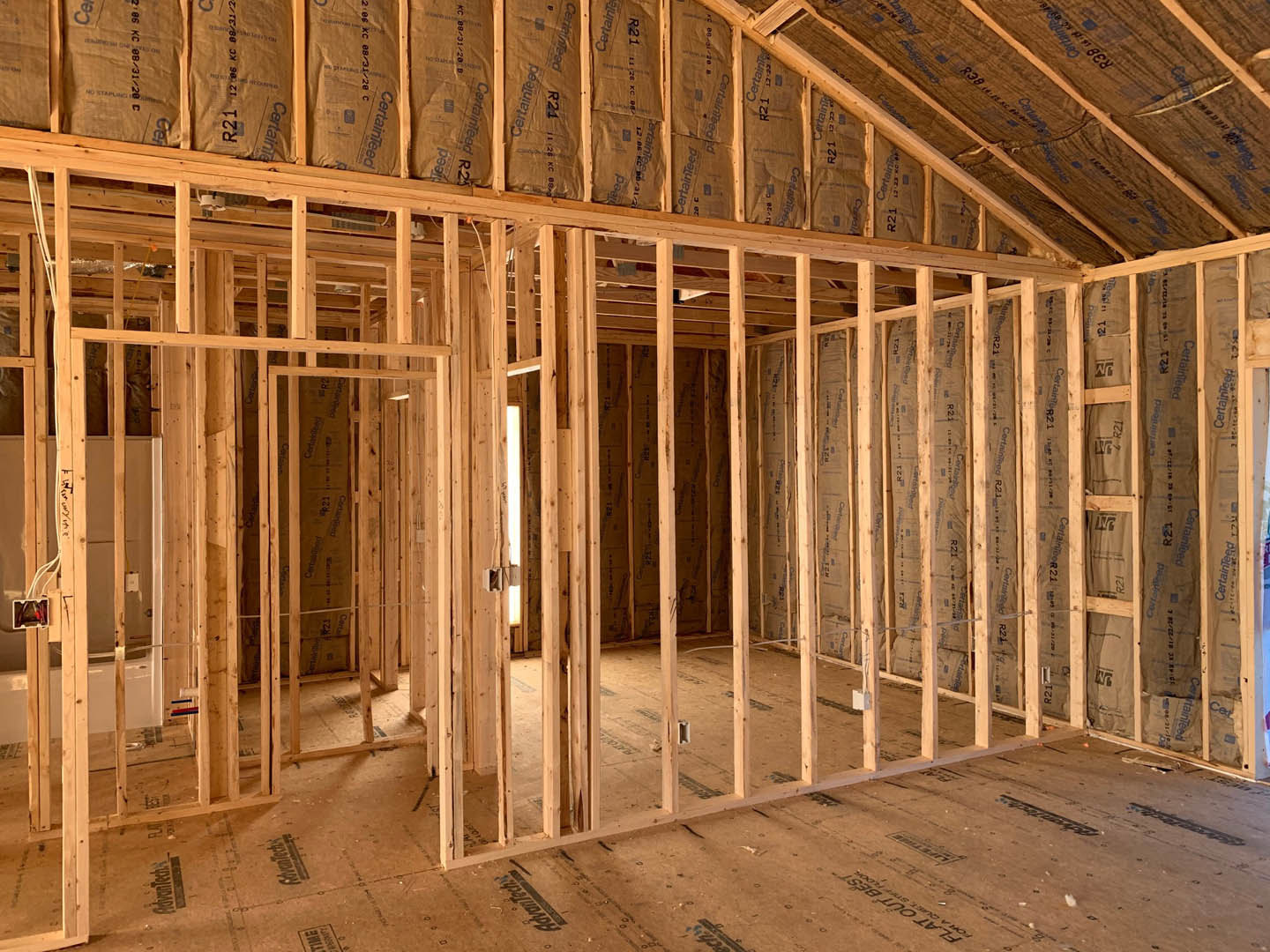 Unfinished room with exposed wood framing, ceiling beams, brown insulation bags, and a white door