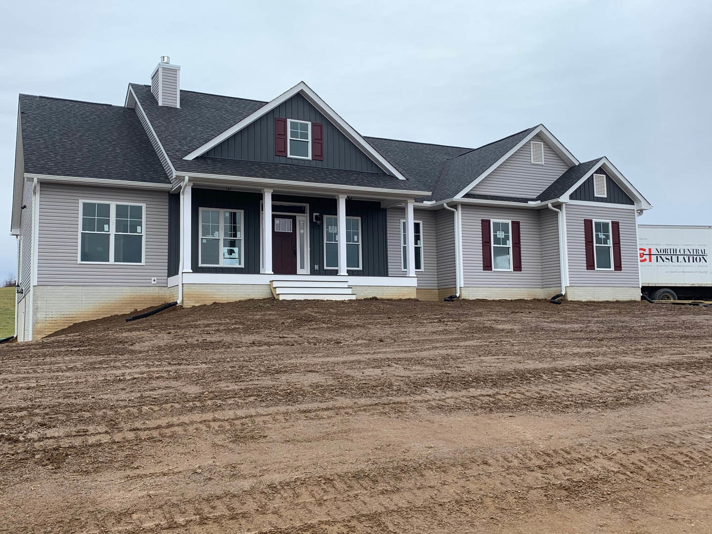 Modern home with white siding and black trim, large windows, dirt yard with tire tracks, truck parked nearby, papers visible in window