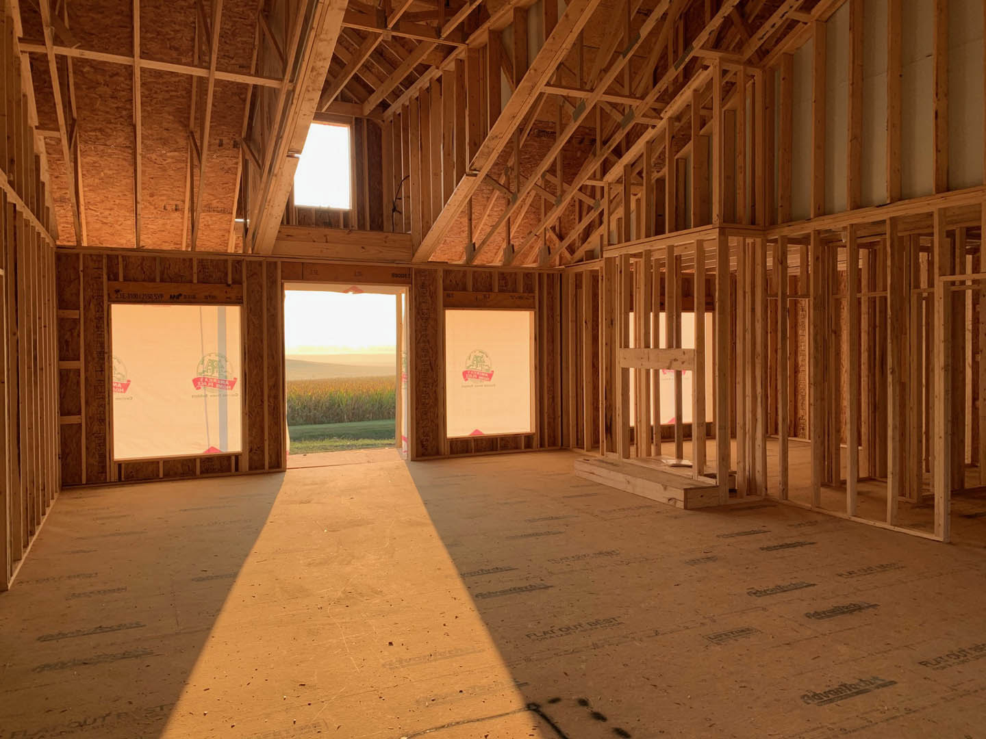 Wooden floor and exposed ceiling beams in a bright room, large window framing a view of a cornfield