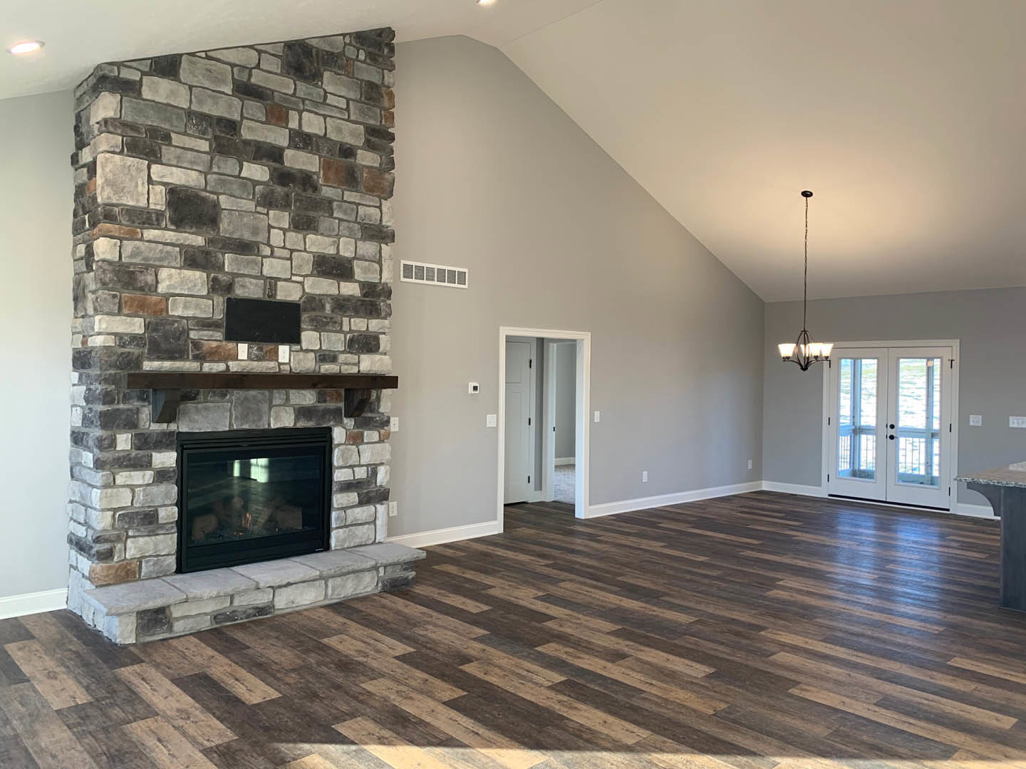 Living room with hardwood floors, stone fireplace featuring a wood mantel and glass door, double glass-paneled doors, white walls, and ceiling.