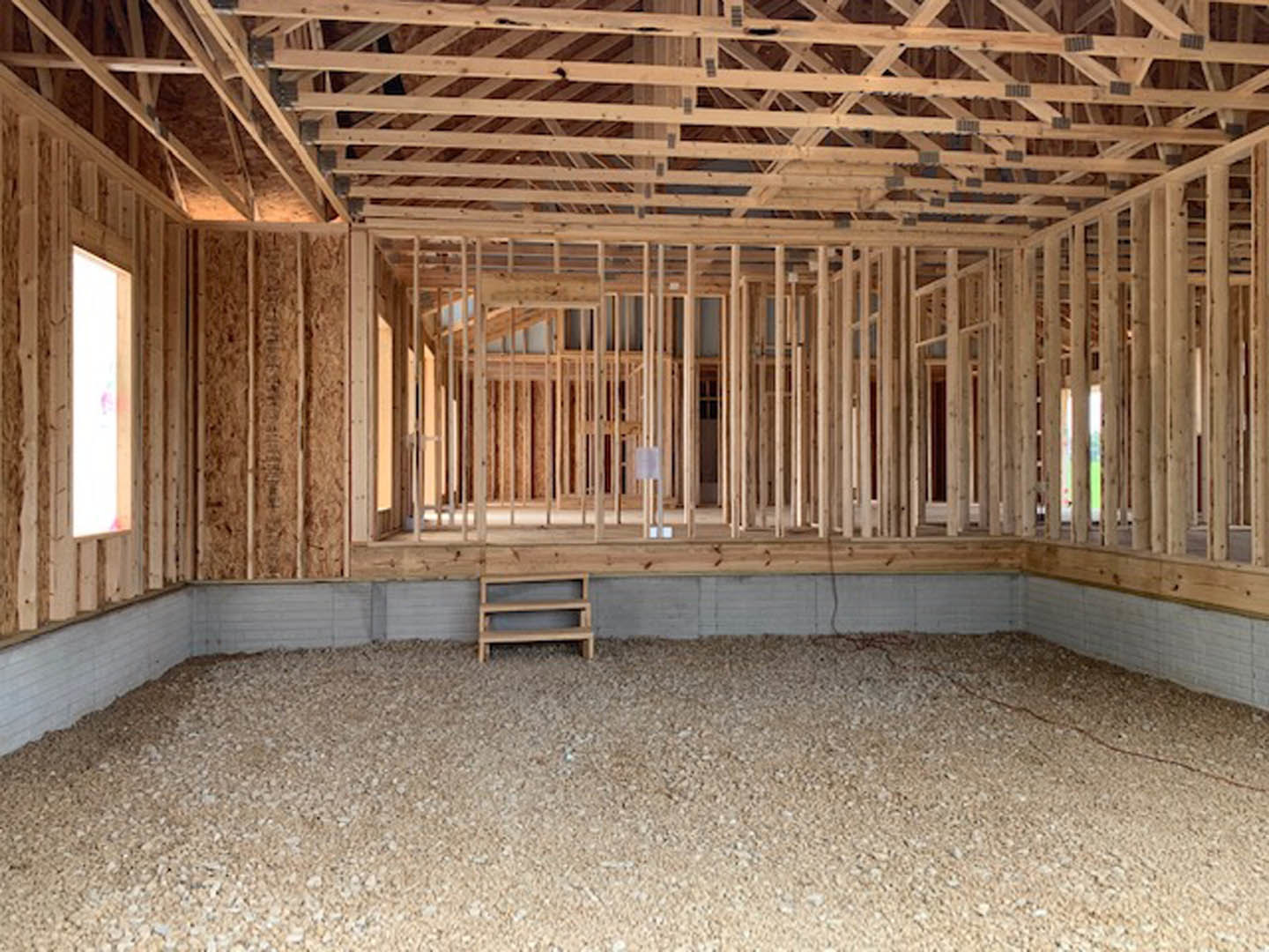 Open room featuring exposed wooden beams, plank ceiling, hardwood flooring, and unfinished lumber framing along the walls.