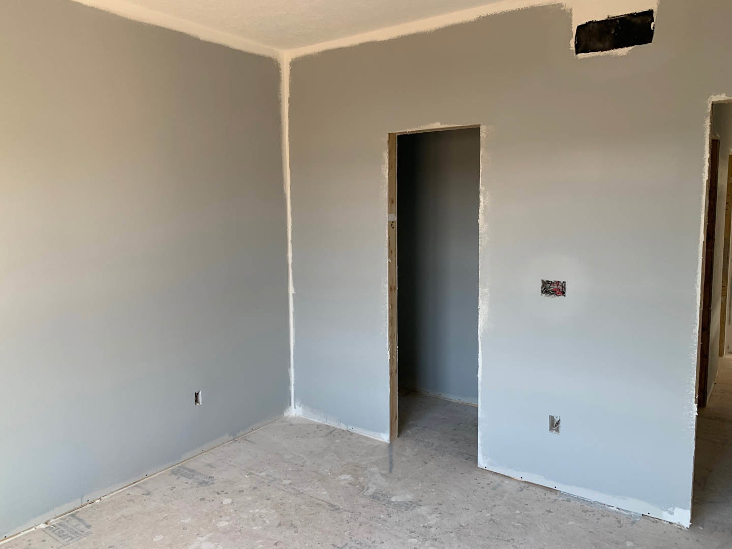 Open white door in modern room, white plaster walls, light switch, white flooring, black rectangular object outside with snow visible through doorway