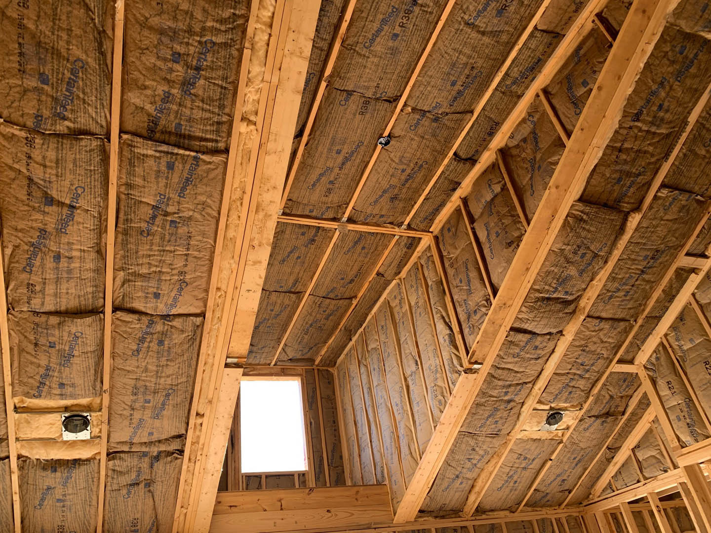 Wooden ceiling with exposed beams, several bags attached, square window, white rectangular object with wood frame, close-up of light fixture, brown paper with blue writing, and