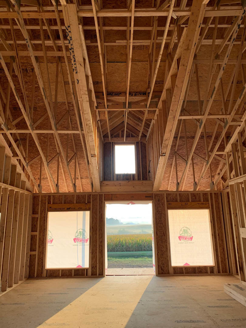 Sunlit room with large windows overlooking a grassy field, wood ceiling beams, and neutral walls