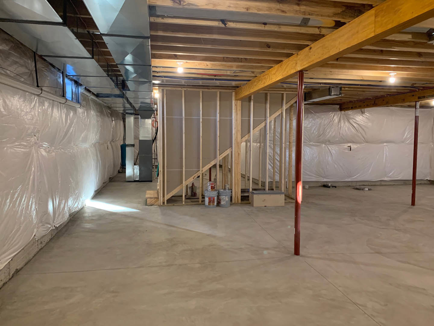 Wooden ceiling with exposed beam, concrete floor with buckets, white wall bordered in brown, pillar close-up, wall covered in plastic, white surface framed in blue