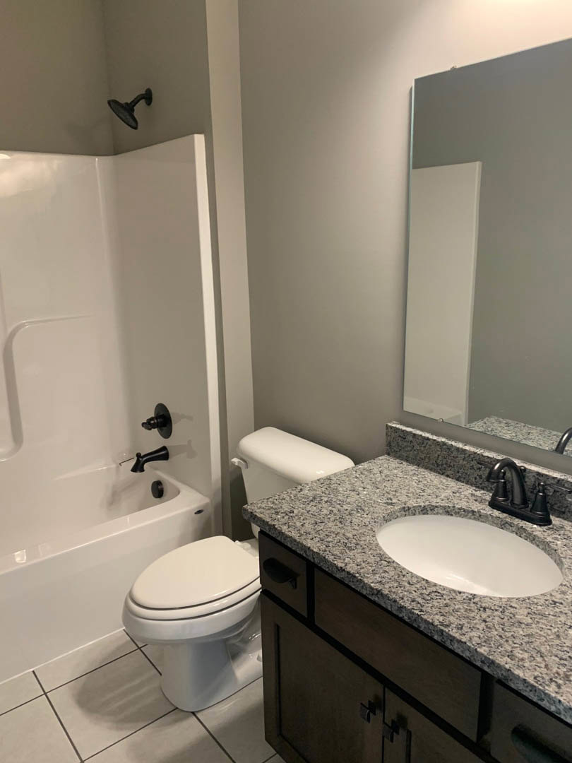 White bathroom with black faucet on rectangular sink, white toilet, light tile walls, and white door visible in foreground