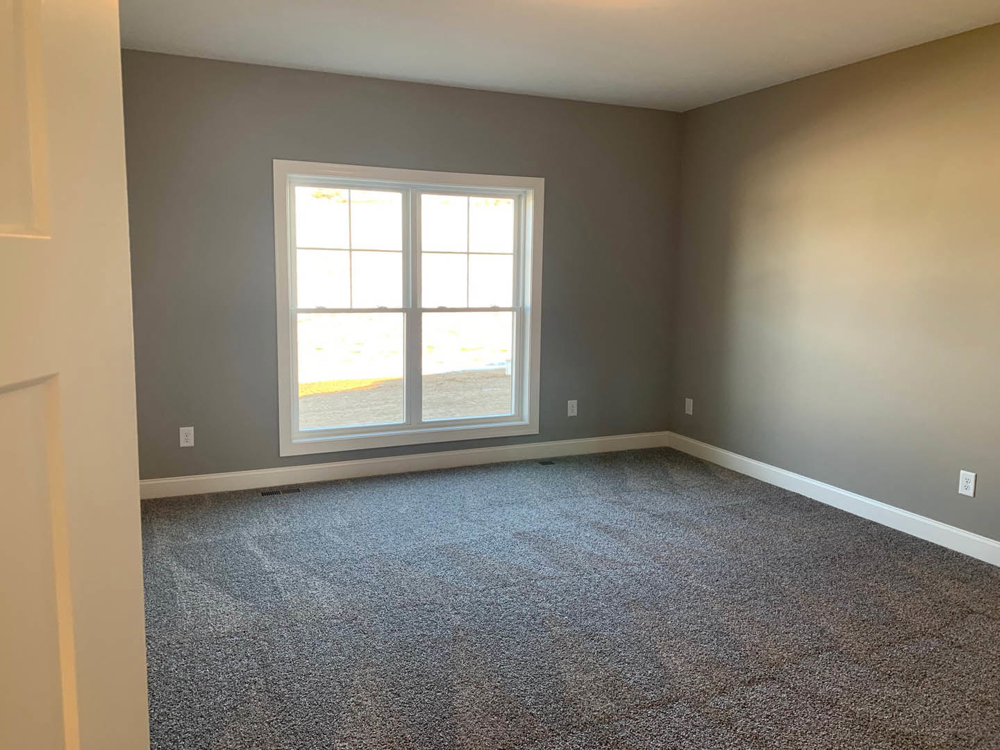 Carpeted room with white walls, black door, white-framed window, floor vent, and baseboard molding