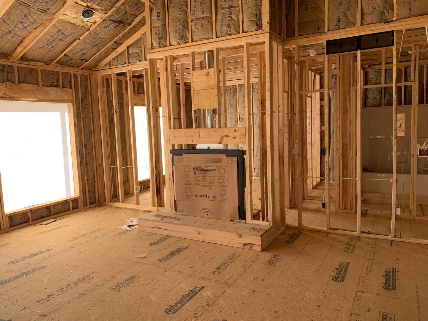 Unfinished room with exposed wood framing, partially installed door, wood planks on floor, cardboard box with instructions, whiteboard with wooden frame, and framed fireplace