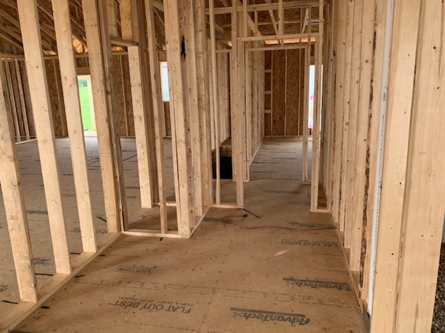 Exposed wood framing and beams inside a partially constructed home, with lumber and insulation materials visible on the unfinished floor.