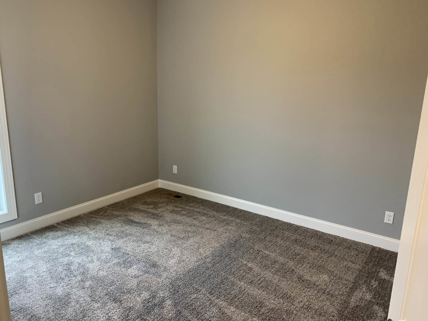 Grey carpeted floor in a room with white walls and a white door frame