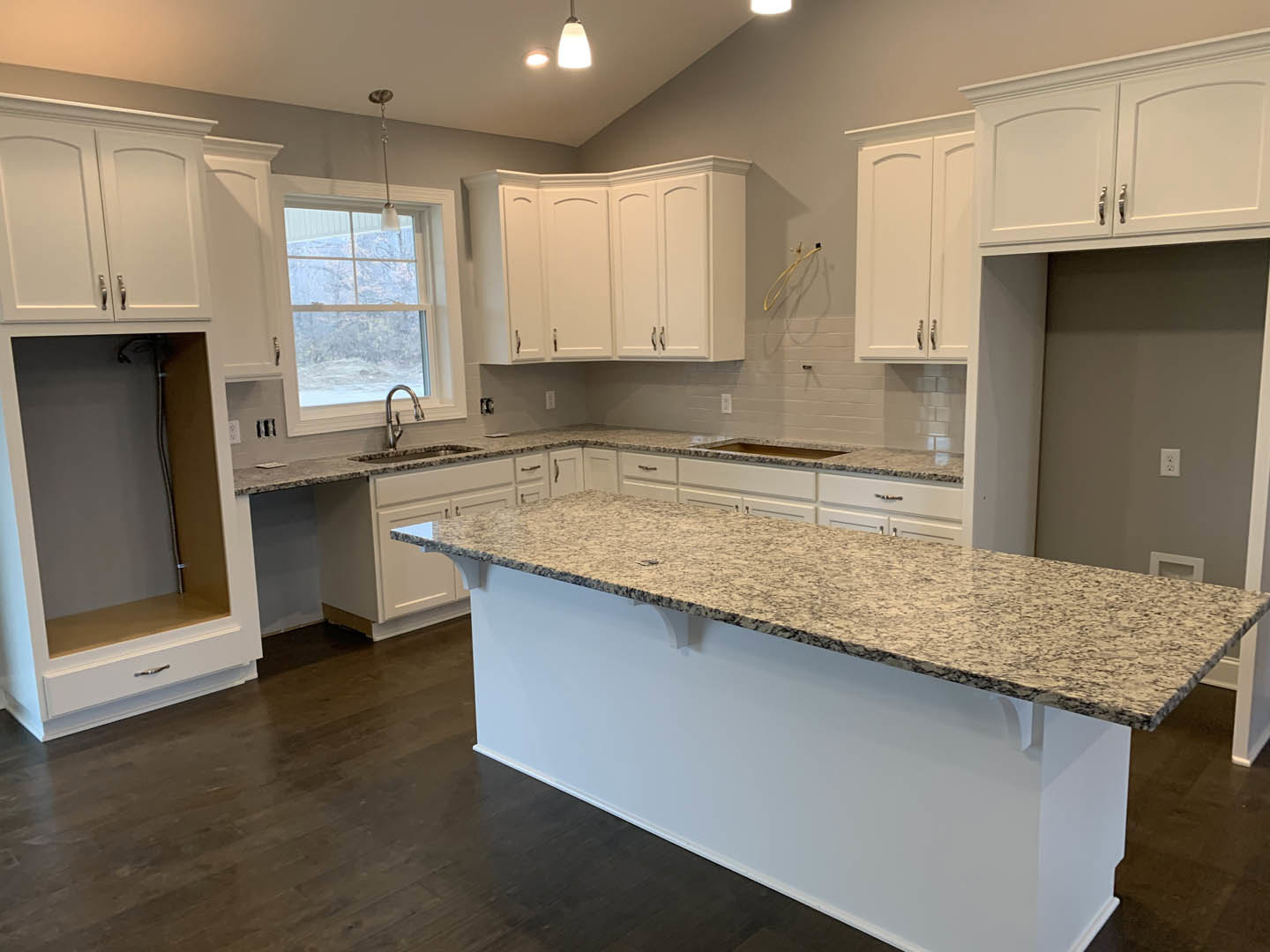 White kitchen cabinets with granite countertops, stainless steel faucet, tile backsplash, pendant light fixture, and window overlooking snowy landscape